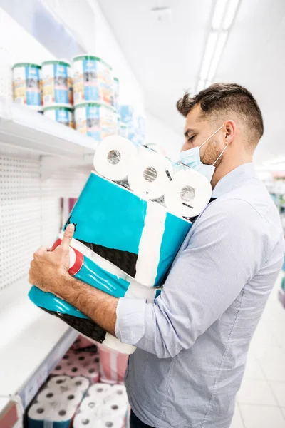 A man is panic buying toilet paper in the supermarket. Stock piling toilet paper rolls at home due to shortage in countries such as Spain, France, Germany, England or Italy