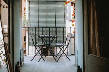 Empty cool and bohemian balcony with chairs and table. There is no people and green wooden blindersin the background. The balcony has opened windows and there is copy space for design. Barcelona.