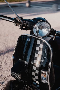 Vertical close up picture of black vintage retro motorbike. There is a square black and white pattern at the front. It second hand and has brown leather seat and a basket at the back.