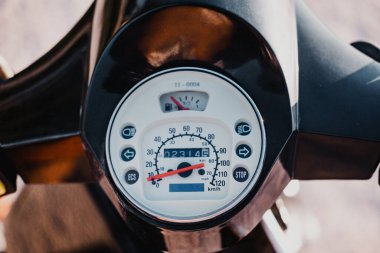 Close up picture of a motorbike dashboard. It's visible the speedometer, lights, stop light, engine or fuel tank.