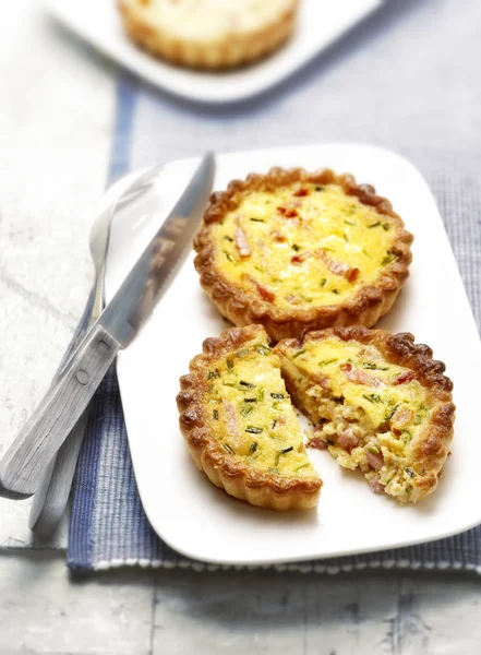 Twee quiches met spek op een plaat een in tweeën gesneden — Stockfoto