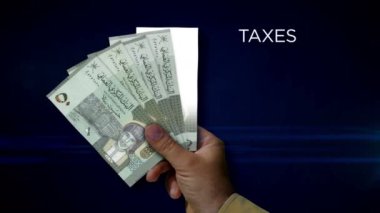 Umman Rial kağıt notu tutuyor. OMR banknotlarının hayranı. Gelir kaybı, yaşam, vergi, kredi ve para kaybı metaforu.