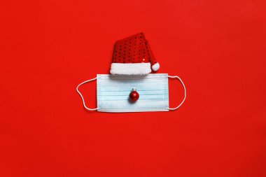 Kırmızı arka planda koruyucu yüz maskesi olan Noel Baba şapkası..