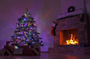 Çiçeklerle süslenmiş bir Noel ağacı ve karanlıkta yanan bir şömine..