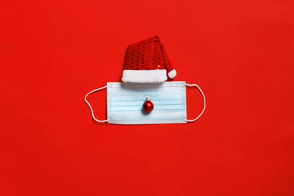 stock image Christmas santa hat with a protective face mask on a red background.