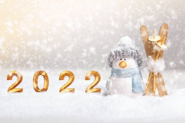 Kış yeni yıl kompozisyonu. 2022 harfli altın ve karda kayak yapan bir penguen..