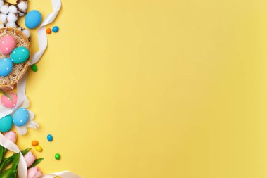 Paskalya kompozisyonu. Sarı arka planda bir sepet lale yumurtası. Kenar düzlüğü üst görünüm kopyalama alanı.