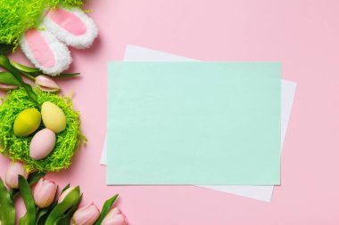 Paskalya kompozisyonu. Lale çiçeği yuvasında çok renkli yumurtalar pembe arka planda tavşan kulakları. Metin ve kopyalama alanı olan boş sayfa