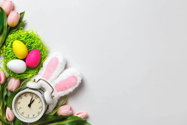 イースターカード 巣の中の多色の卵花チューリップは灰色の背景にウサギの耳で目覚まし時計 コピースペース — ストック写真