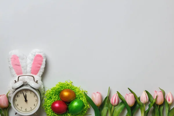 イースターのコンセプト 灰色の背景に花のチューリップの巣の中にウサギの真珠の卵の耳の中に目覚まし時計 コピースペース — ストック写真