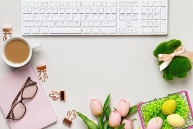 Masaüstü. Paskalya süslemeleri olan bir masada bardak kahve fincanı klavye defteri. Üst görünüm düz kopya alanı
