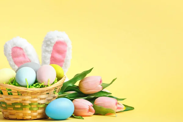 イースターの構図 黄色の背景にバスケットチューリップウサギの耳の中の卵 — ストック写真