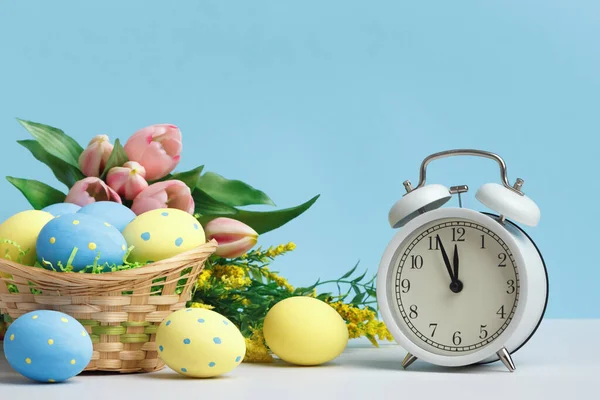 イースターのコンセプト 卵のバスケットは 青い背景コピースペース上のクロック花を目覚まし時計 — ストック写真