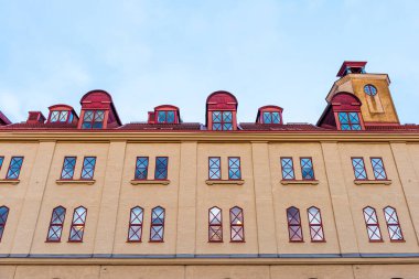 Pencereli bej tuğla bina, kırmızı çatı ve mavi gökyüzü.