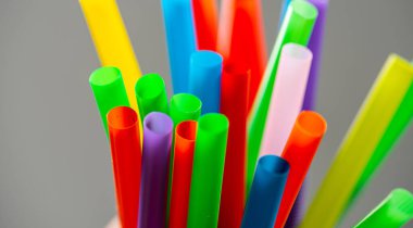 Gri arkaplanın önündeki kavanozda çok renkli plastik pipetler..