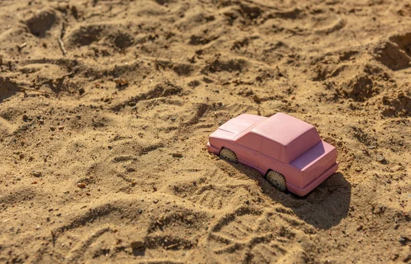 Pink toy car in the sand at a playground.