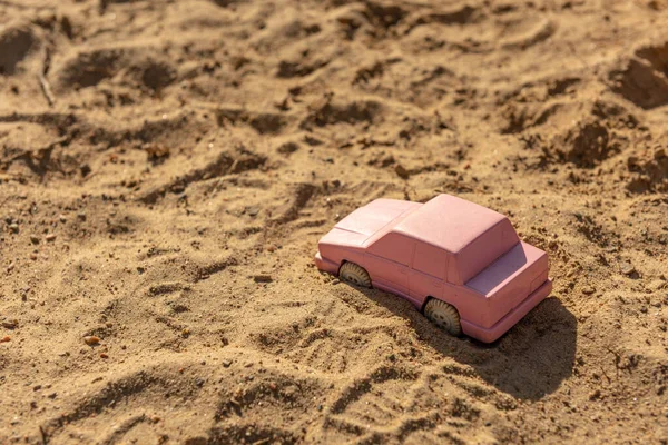 Pink toy car in the sand at a playground.