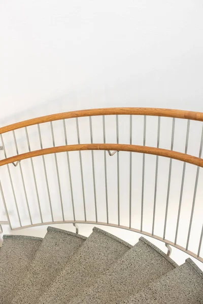 Spiral stairs with wooden railings along a white wall.
