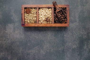 Yeşil ve kahverengi kavrulmamış ve kavrulmuş kahve çekirdekleri, koyu beton arka planda kepçelerle ahşap kutuda..