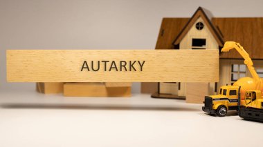 The word Autarky is written on the wooden surface. House and construction concept in background . Mortgage and economy