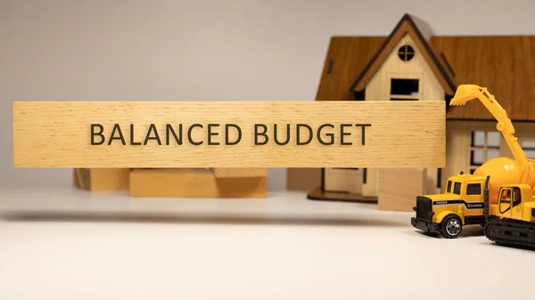 The word Balanced budget is written on the wooden surface. House and construction concept in background . Mortgage and economy