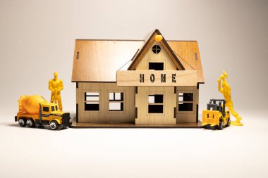 The word Home is written on the wooden surface. Workers working on wooden miniature house in the background. business and finance