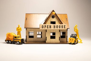 Open house word written on wooden surface. Workers working on wooden miniature house in the background. business and finance