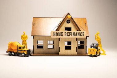 The word Home refinance is written on the wooden surface. Workers working on wooden miniature house in the background. business and finance