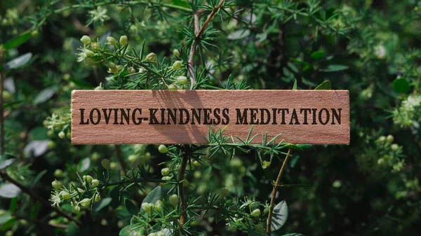 Loving, Kindness meditation. Written on wooden surface. Background tree leaves. Mental health and lifestyle.