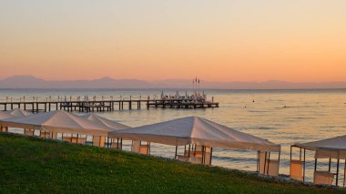 Akşamın arka planında beyaz bir çardağı olan eski bir metal iskele sakin bir deniz.