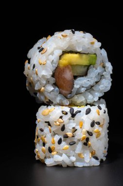 Siyah arka planda uramaki somonu, avokado ve salatalık.