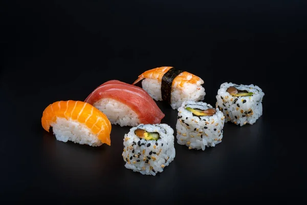 varied sushi ration with black background and props