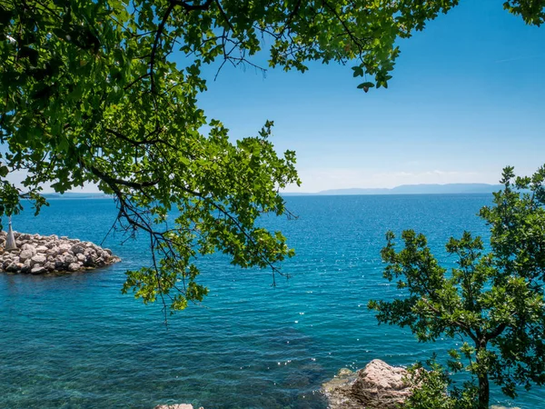 Hırvatistan 'ın Kostrena kentinde mavi ve yeşil deniz, güzel plaj ve yeşil ağaçlar.