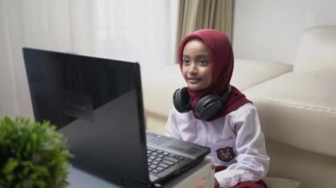 tesettürlü bir ilkokul öğrencisi dizüstü bilgisayar ve kulaklık kullanarak bir video görüşmesi yapmış.