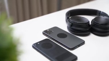 Koyu renk akıllı telefon ve kulaklıklar beyaz bir masada.
