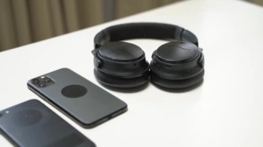 Koyu renk akıllı telefon ve kulaklıklar beyaz bir masada.