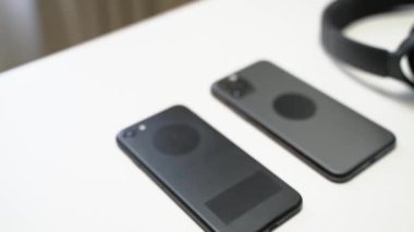 İki siyah akıllı telefonun ve kulaklığın videosunu beyaz bir masada kapat.