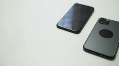 Beyaz masadaki iki siyah akıllı telefonun videosunu kapat.