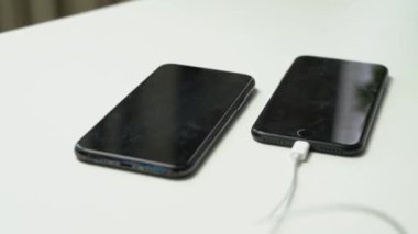 Biri beyaz masaya beyaz kulaklık takan iki siyah akıllı telefonun videosunu kapat.