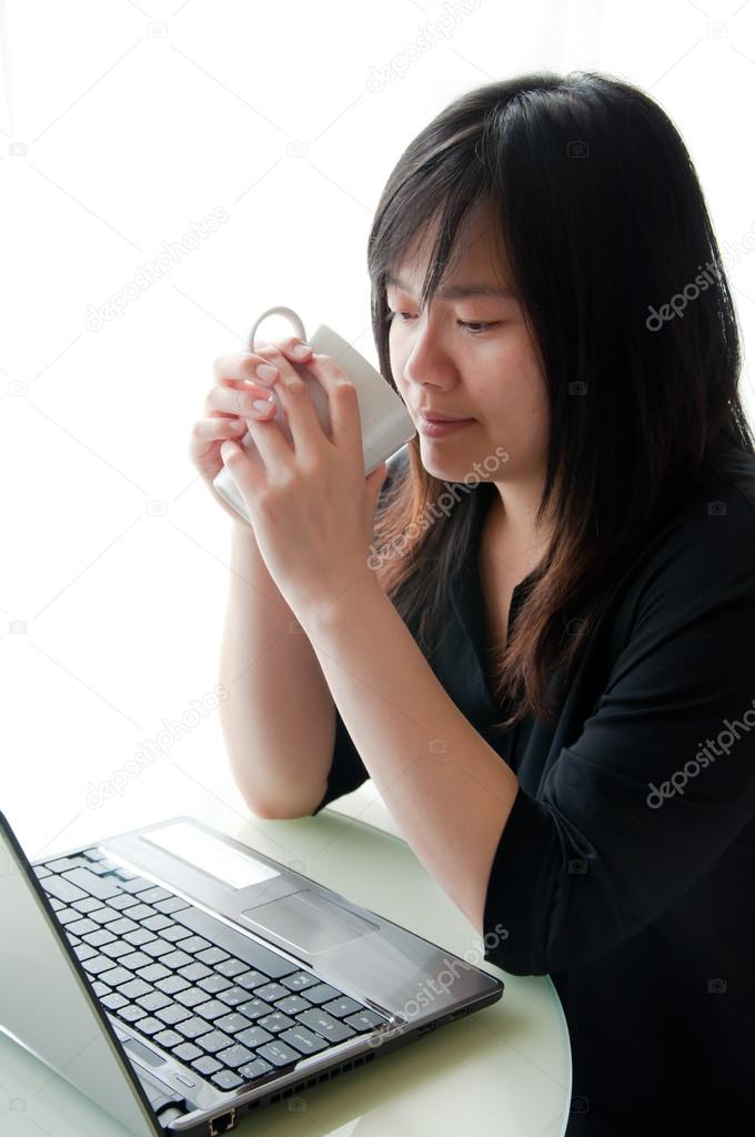 An asian woman works with computer and coffee cup