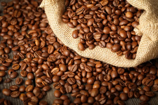 Grains de café dans un sac à café en toile de jute sur une surface en bois . — Photo