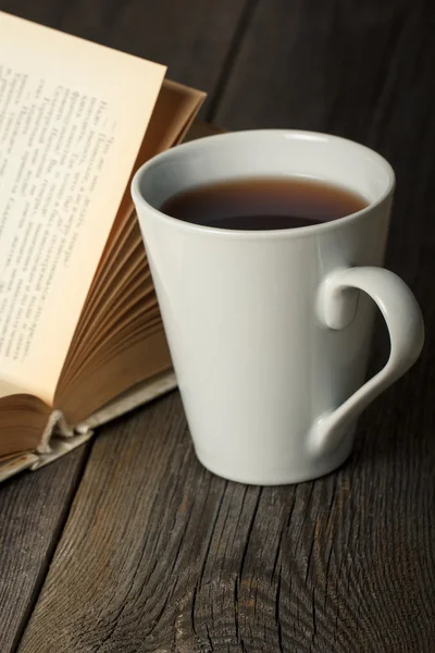 Φλιτζάνι τσάι με παλιά άνοιξε βιβλίο για ξύλινο τραπέζι — Φωτογραφία Αρχείου