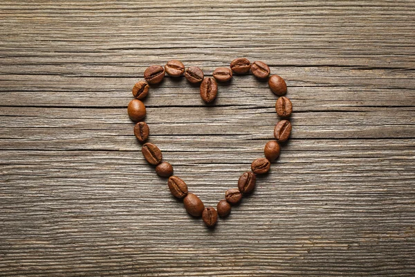 Heart shape made from coffee beans on wooden table. — Stock Photo, Image