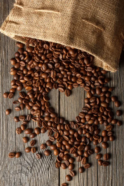 Forma de corazón hecha de granos de café en textura de madera o mesa con bolsa de café . — Foto de Stock