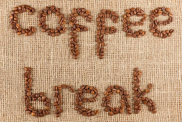 Coffee brake title laid out from coffee beans on a burlap pattern. — Stock Photo, Image