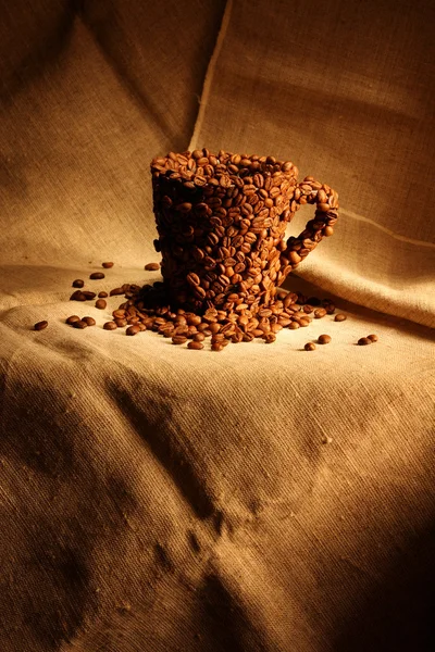 Image of mug covered with coffee beans on canvas background — Stock Photo, Image