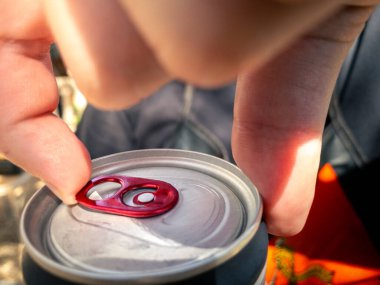 Soda ya da bira kutusunu tutan ve açan adama yakın çekim. Eller alüminyum bir içeceği açar. Dışında güneş ışığı olan kola kutuları içerler.
