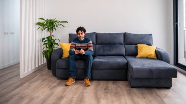 Kafkasyalı bir adamın portresi akıllı telefon kullanarak güzel bir iç mekanda koltukta oturuyor. Beyaz adam telefon cihazını evin kanepesinde kontrol ediyor..