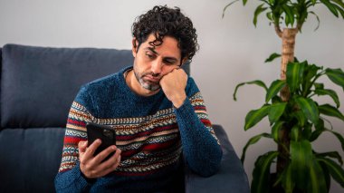 Erkek depresyonu ve kanepede oturmak. Sakallı yetişkin adam akıllı telefonunu kullanıyor ve düşünüyor, ağır düşünceleri var, sevgilisinden ya da maddi zorluklar kavramından ayrılıyor.
