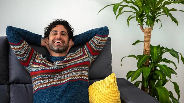 Portrait of happy latin man in casual relaxing on couch and smiling. Cheerful caucasian guy looking at camera. Satisfied man feeling confident in a sofa home